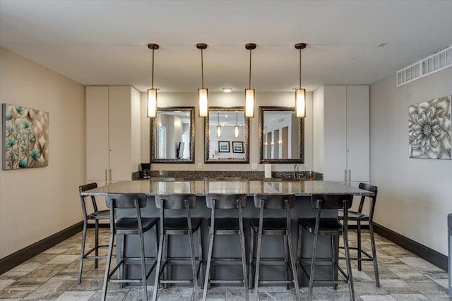 kitchen with baseboards, light stone counters, visible vents, and a breakfast bar area