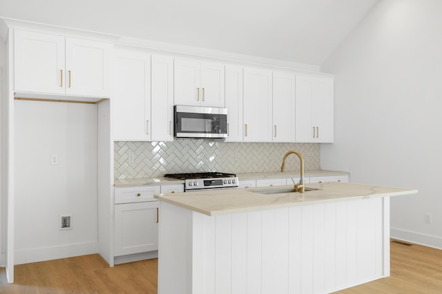 kitchen with range with gas cooktop, a sink, a kitchen island with sink, stainless steel microwave, and backsplash