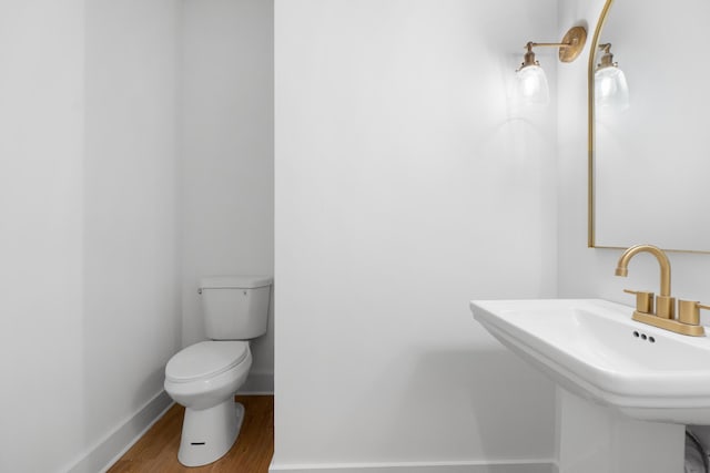 half bath featuring baseboards, toilet, wood finished floors, and a sink