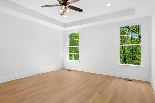 spare room with baseboards, light wood-style flooring, visible vents, and a tray ceiling