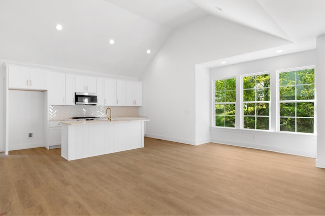 kitchen with white cabinets, decorative backsplash, an island with sink, light countertops, and stainless steel microwave