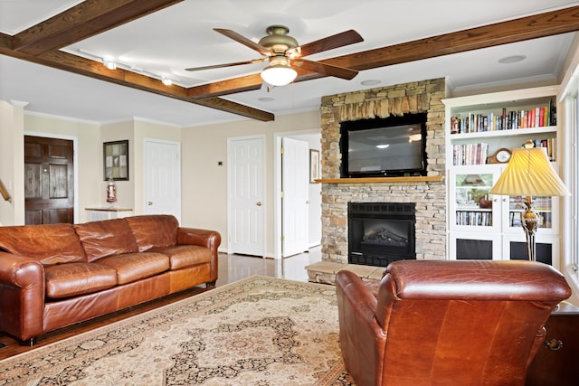 living area featuring beam ceiling, a ceiling fan, wood finished floors, crown molding, and a stone fireplace
