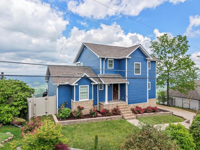 traditional-style home featuring a gate, a front lawn, fence, and a shingled roof