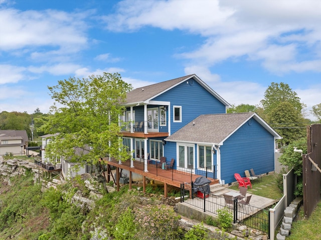 back of property with roof with shingles, fence, a wooden deck, a patio area, and a balcony
