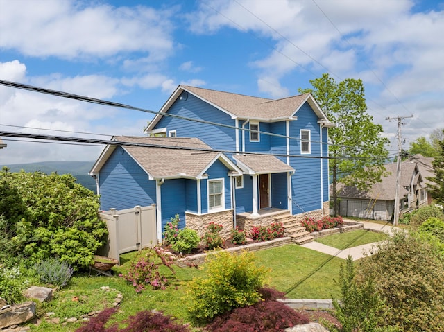 craftsman-style house featuring fence, stone siding, roof with shingles, and a front yard