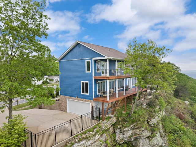 rear view of property with stone siding, concrete driveway, fence, a garage, and a balcony