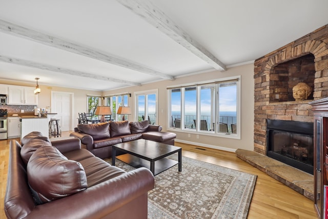 living room with beamed ceiling, light wood-type flooring, a wealth of natural light, and a large fireplace