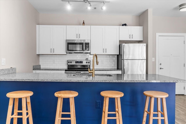 kitchen with tasteful backsplash, stainless steel appliances, white cabinetry, and a sink
