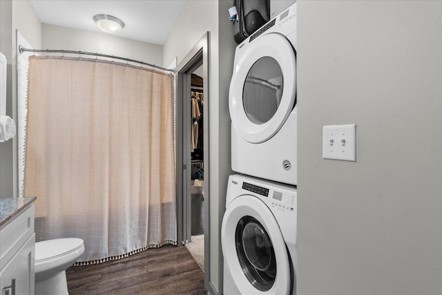 clothes washing area featuring dark wood-type flooring, stacked washing maching and dryer, and laundry area