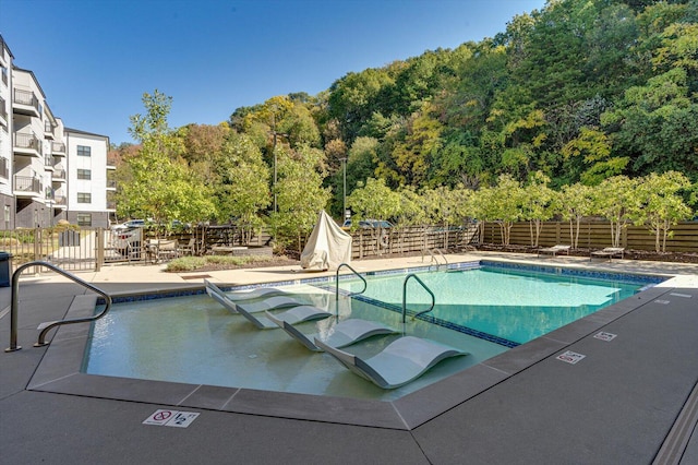community pool featuring fence, a patio area, and a wooded view