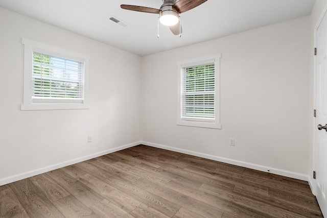 empty room with plenty of natural light, visible vents, wood finished floors, and a ceiling fan