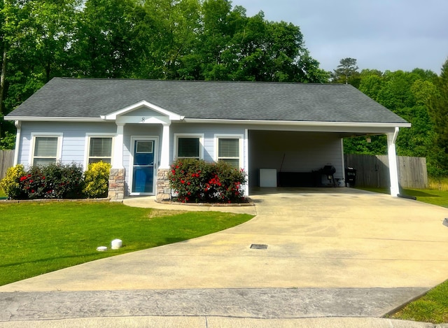 view of front of home with fence, roof with shingles, an attached carport, a front yard, and concrete driveway