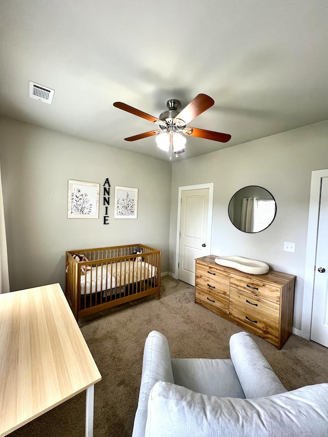 bedroom with a ceiling fan, visible vents, carpet floors, baseboards, and a crib