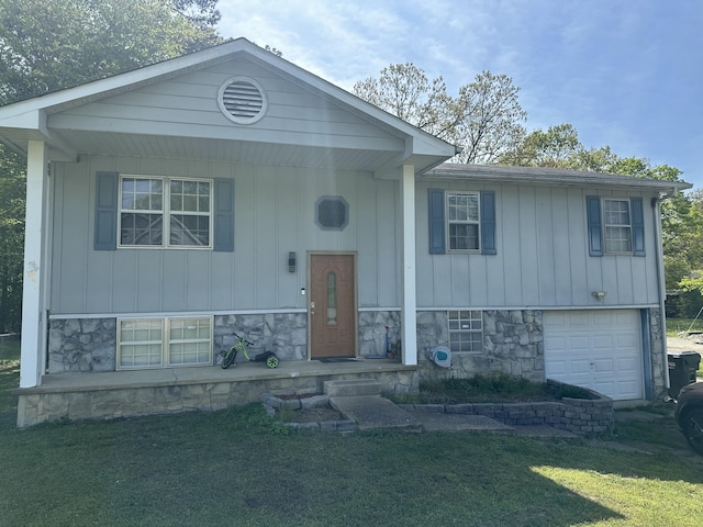 bi-level home featuring an attached garage, stone siding, and a front lawn