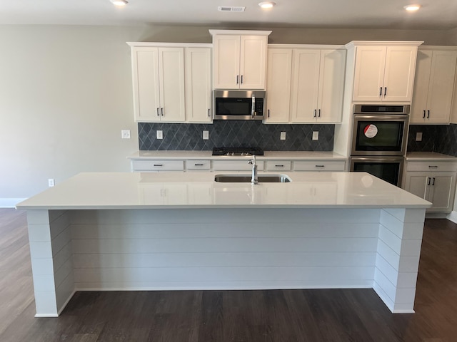kitchen featuring an island with sink, light countertops, backsplash, a sink, and appliances with stainless steel finishes