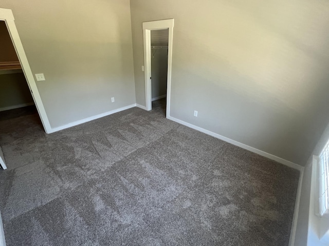 unfurnished bedroom with a spacious closet, baseboards, dark colored carpet, and a closet