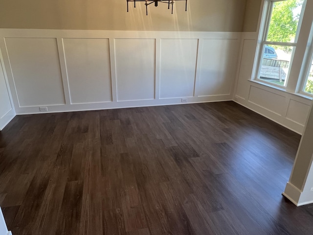 unfurnished dining area with a wainscoted wall, dark wood-style flooring, and a decorative wall