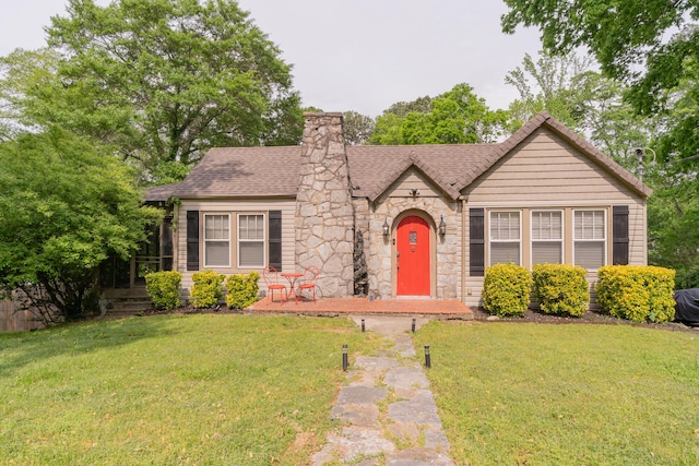 tudor home featuring a chimney, stone siding, a front yard, and a shingled roof