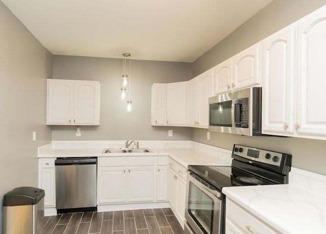 kitchen with stainless steel appliances, a sink, pendant lighting, wood finish floors, and white cabinetry