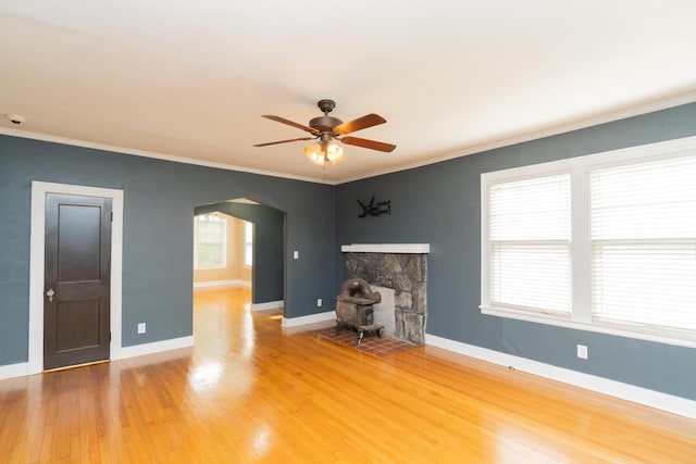 unfurnished living room featuring arched walkways, baseboards, a ceiling fan, wood finished floors, and ornamental molding