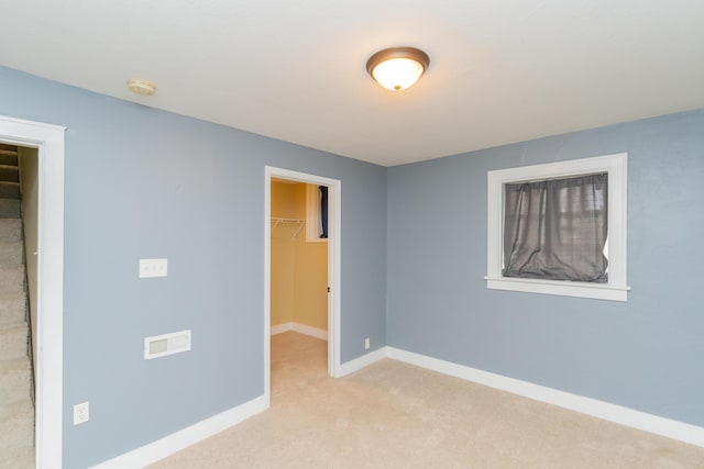 unfurnished bedroom with a closet, a walk in closet, carpet, baseboards, and visible vents
