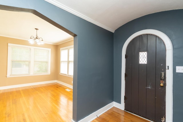 foyer with wood finished floors, arched walkways, crown molding, baseboards, and a chandelier