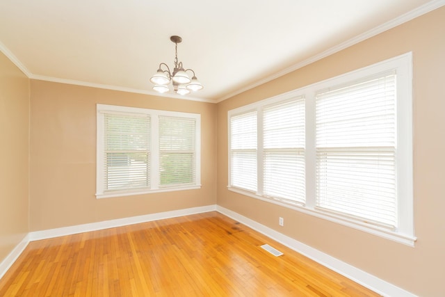 empty room with crown molding, light wood-type flooring, baseboards, a notable chandelier, and visible vents