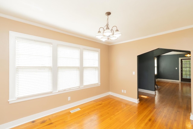spare room with visible vents, light wood-type flooring, crown molding, baseboards, and a notable chandelier
