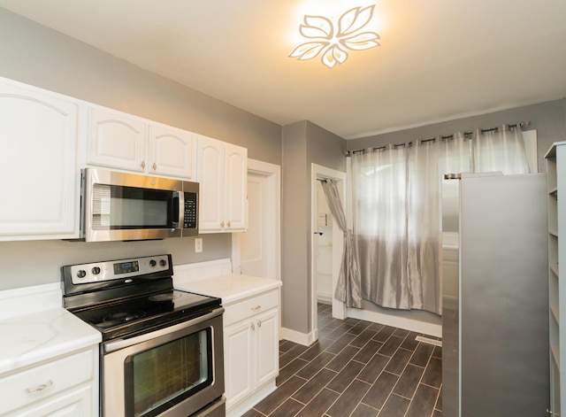 kitchen featuring stainless steel appliances, light countertops, dark wood-type flooring, baseboards, and white cabinetry