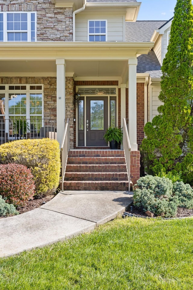 entrance to property with a porch, a shingled roof, and stone siding