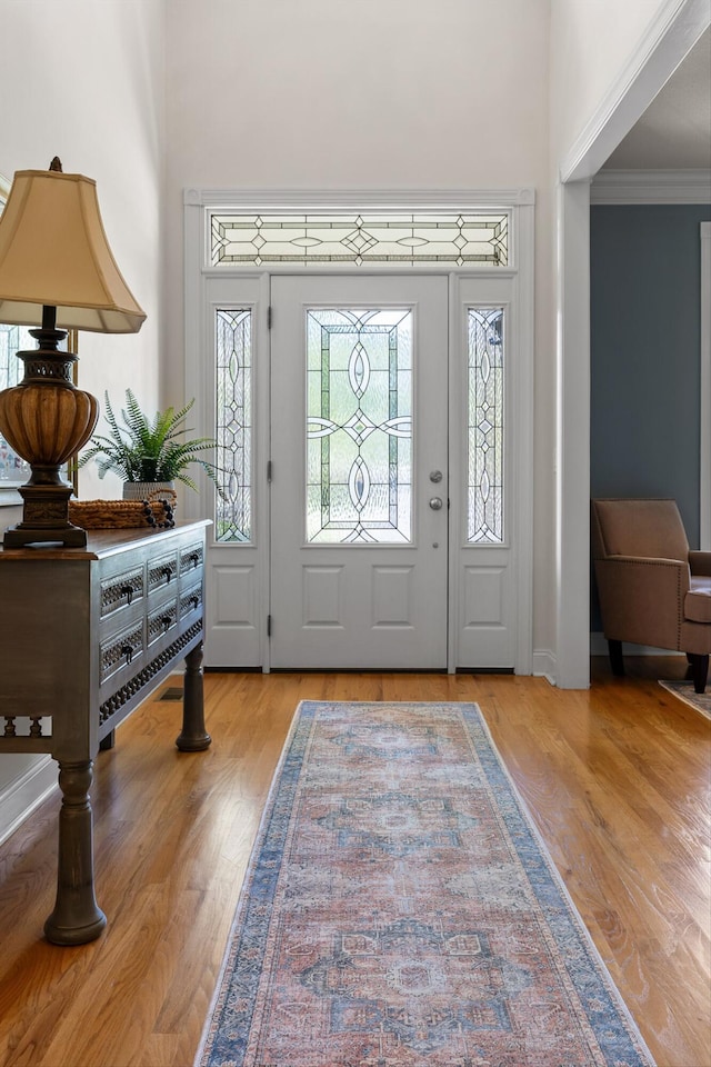foyer entrance with ornamental molding, wood finished floors, and a towering ceiling