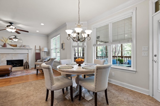 dining room featuring crown molding, a tile fireplace, light tile patterned floors, baseboards, and ceiling fan with notable chandelier