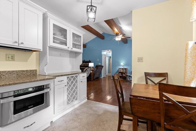kitchen featuring vaulted ceiling with beams, white cabinetry, stainless steel oven, and stone counters