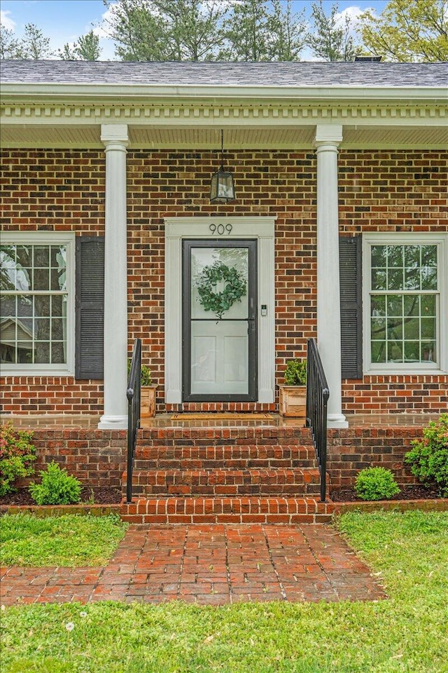 view of exterior entry with brick siding and a porch