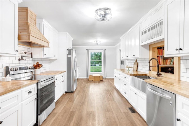 kitchen with visible vents, baseboards, premium range hood, light wood-type flooring, and stainless steel appliances