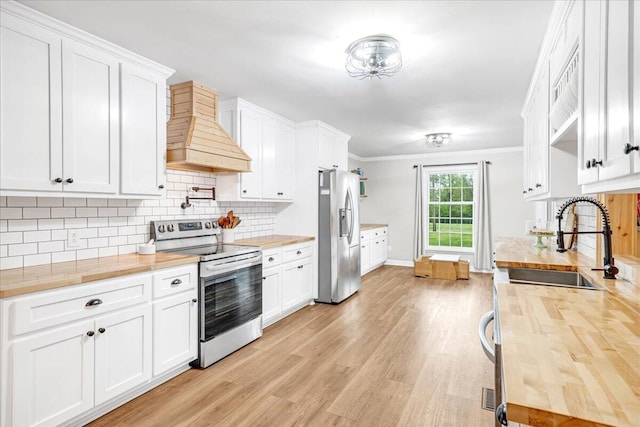 kitchen featuring appliances with stainless steel finishes, a sink, wood counters, custom range hood, and light wood-type flooring