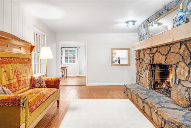 living room with crown molding, baseboards, a stone fireplace, and hardwood / wood-style floors