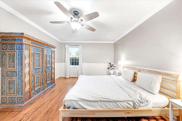 bedroom with ornamental molding, a ceiling fan, wainscoting, and light wood finished floors