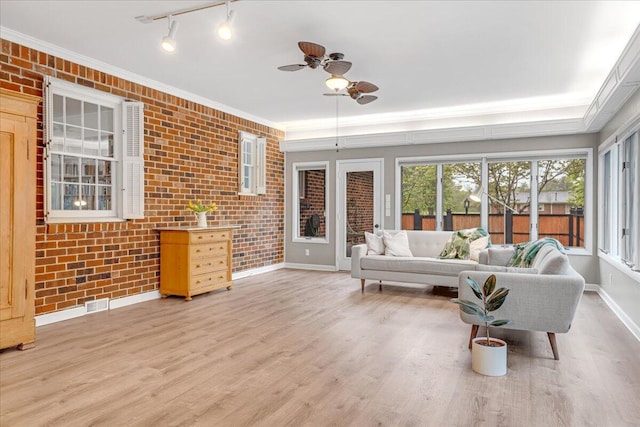interior space with baseboards, a ceiling fan, brick wall, and light wood-type flooring