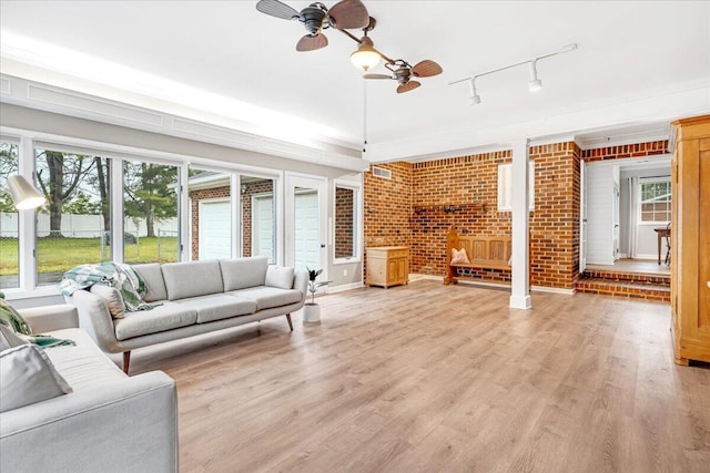 living area with track lighting, a ceiling fan, brick wall, and light wood-type flooring