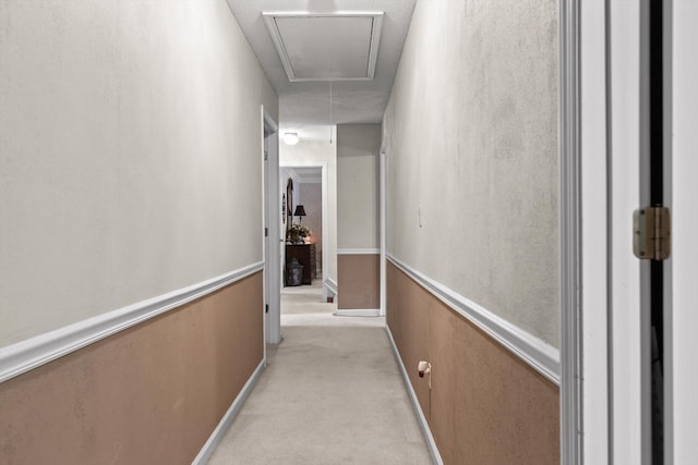 hall with attic access, light carpet, and baseboards