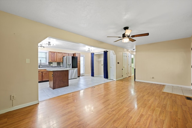 unfurnished living room featuring arched walkways, ceiling fan, light wood-style flooring, and baseboards