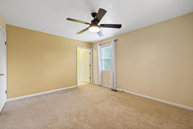 empty room with baseboards, visible vents, ceiling fan, and light colored carpet