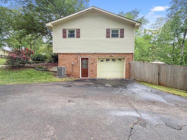 exterior space featuring fence, central AC unit, aphalt driveway, and brick siding