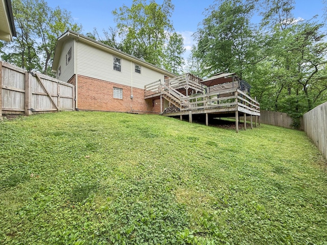 rear view of property with stairs, a wooden deck, a lawn, brick siding, and a fenced backyard