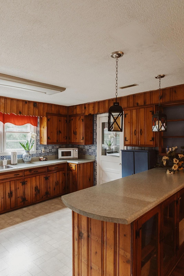 kitchen with brown cabinets, a textured ceiling, pendant lighting, and white microwave