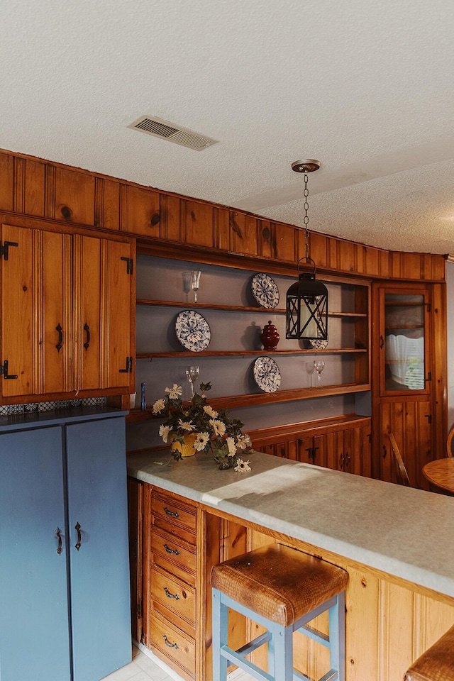 interior space with a textured ceiling, visible vents, open shelves, brown cabinets, and light countertops