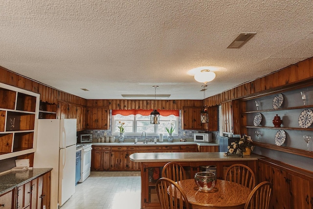 kitchen with visible vents, a peninsula, white appliances, wooden walls, and a sink