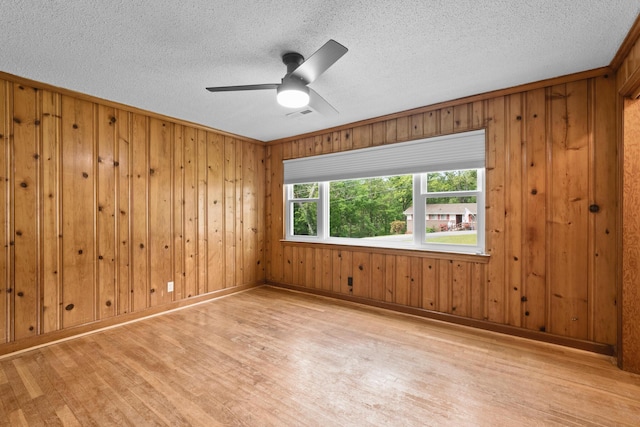 empty room featuring light wood-style floors, a ceiling fan, wood walls, and visible vents