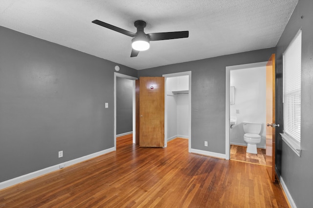 unfurnished bedroom featuring wood finished floors, baseboards, a closet, connected bathroom, and a spacious closet